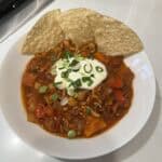 Picture of a bowl of Instant Pot Turkey Chili topped with sour cream and green onions and garnished with tortilla chips.