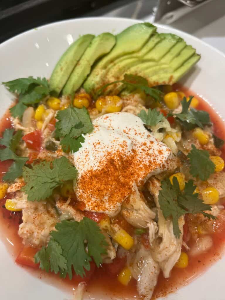 Picture of a bowl of white bean chicken tortilla soup topped with avocado, sour cream, and cilantro
