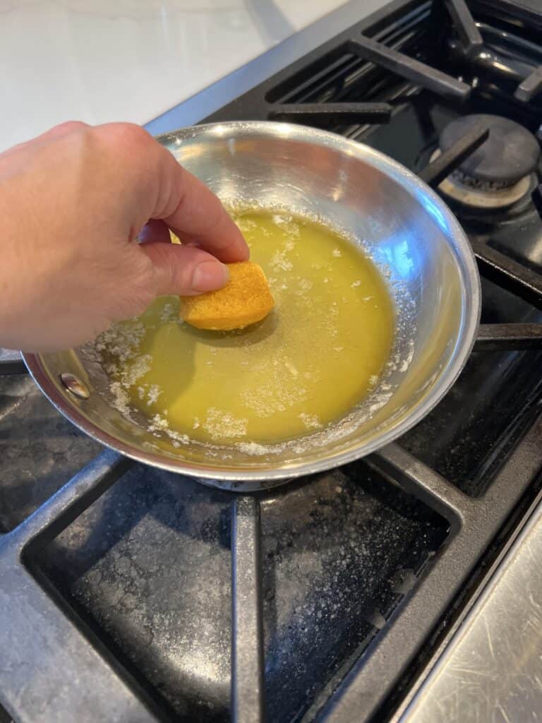 Picture of a Baked Apple Cinnamon Doughnut Hole being dipped into melted butter. 