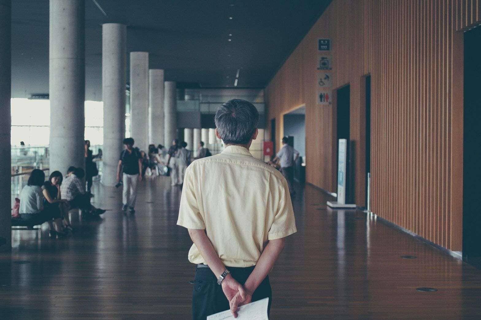 Personas en un aeropuerto, esperando en la sala de espera, ambiente moderno con columnas de concreto y paredes de madera.