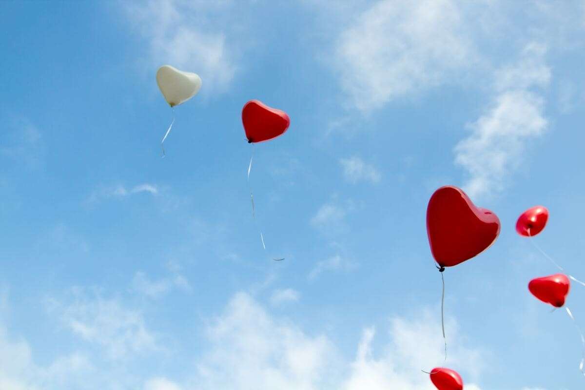 Corazón en globos flotando en cielo azul con nubes, símbolo del amor.