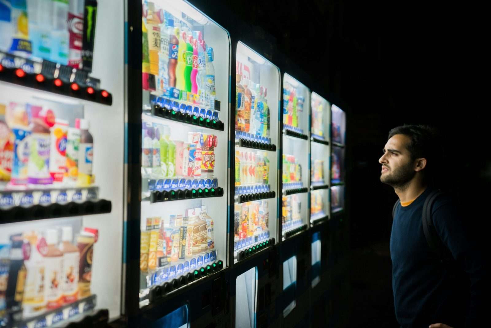 Vendedor observando máquinas expendedoras con bebidas en una tienda nocturna.