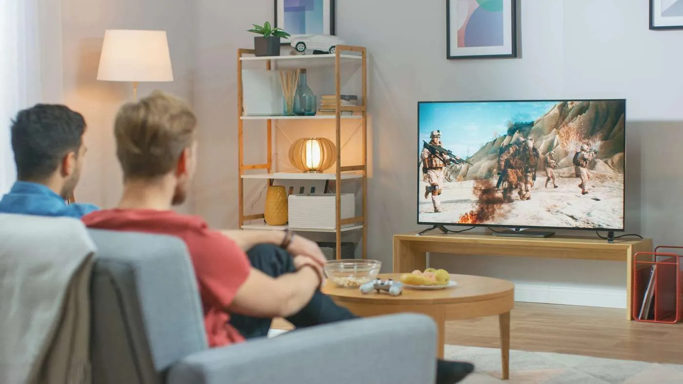 Video de personas viendo televisión con videojuegos de combate en un salón moderno.