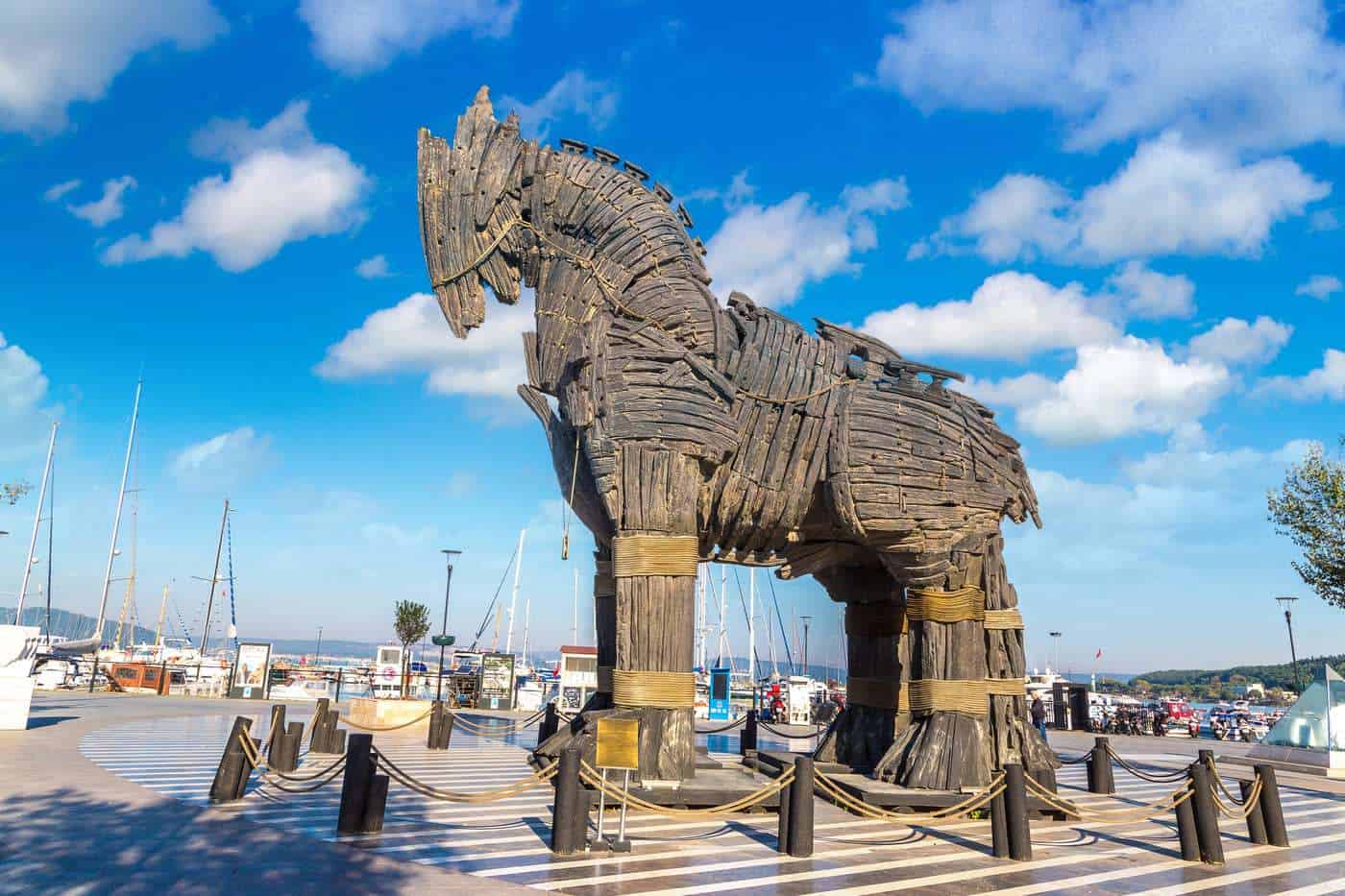 Caballo de madera gigante en puerto con barcos y cielo azul despejado.