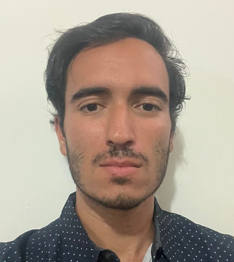 Un hombre con barba y pelo oscuro, usando camisa azul con puntos blancos, retrato en interior.