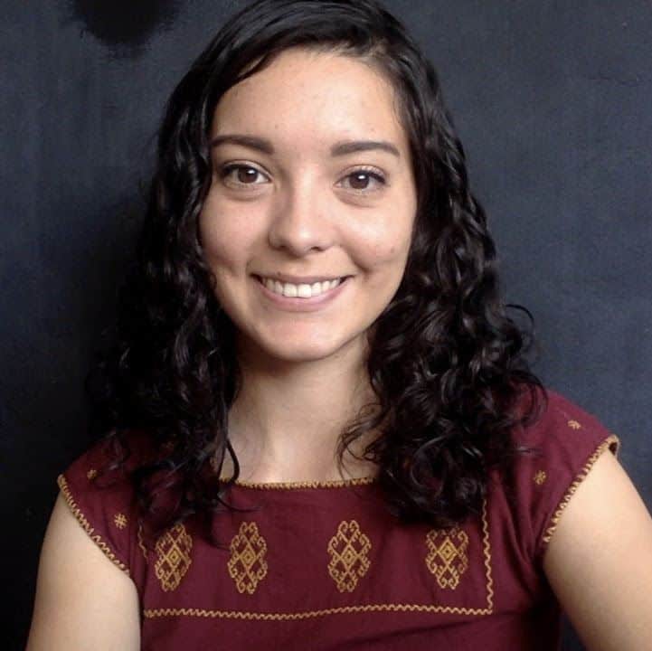 Pensadora joven con cabello rizado y sonrisa amigable, en fondo oscuro.