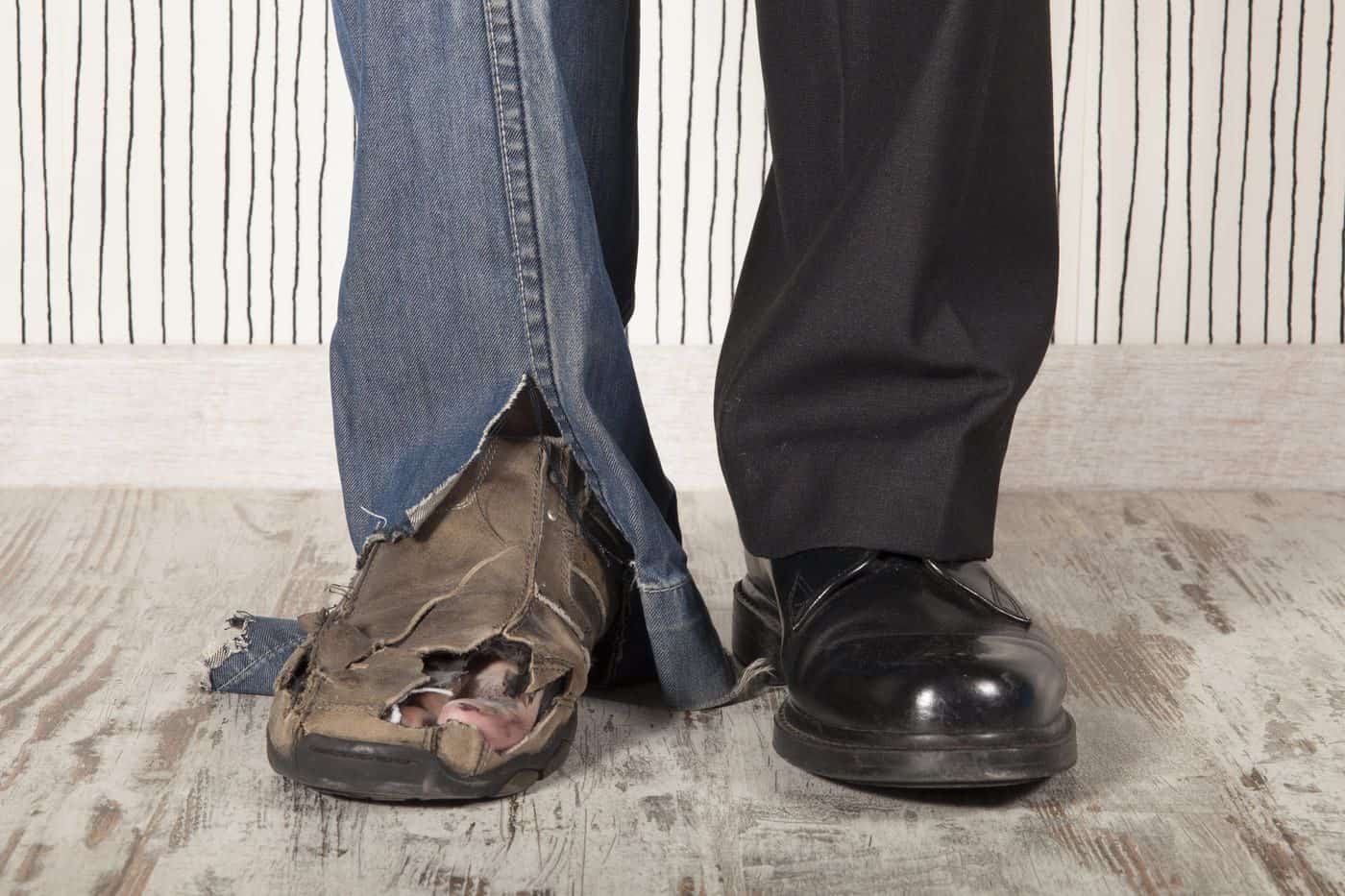 Desgaste del zapato izquierdo y calzado formal en el pie derecho en una persona con pantalones oscuros y casuales.