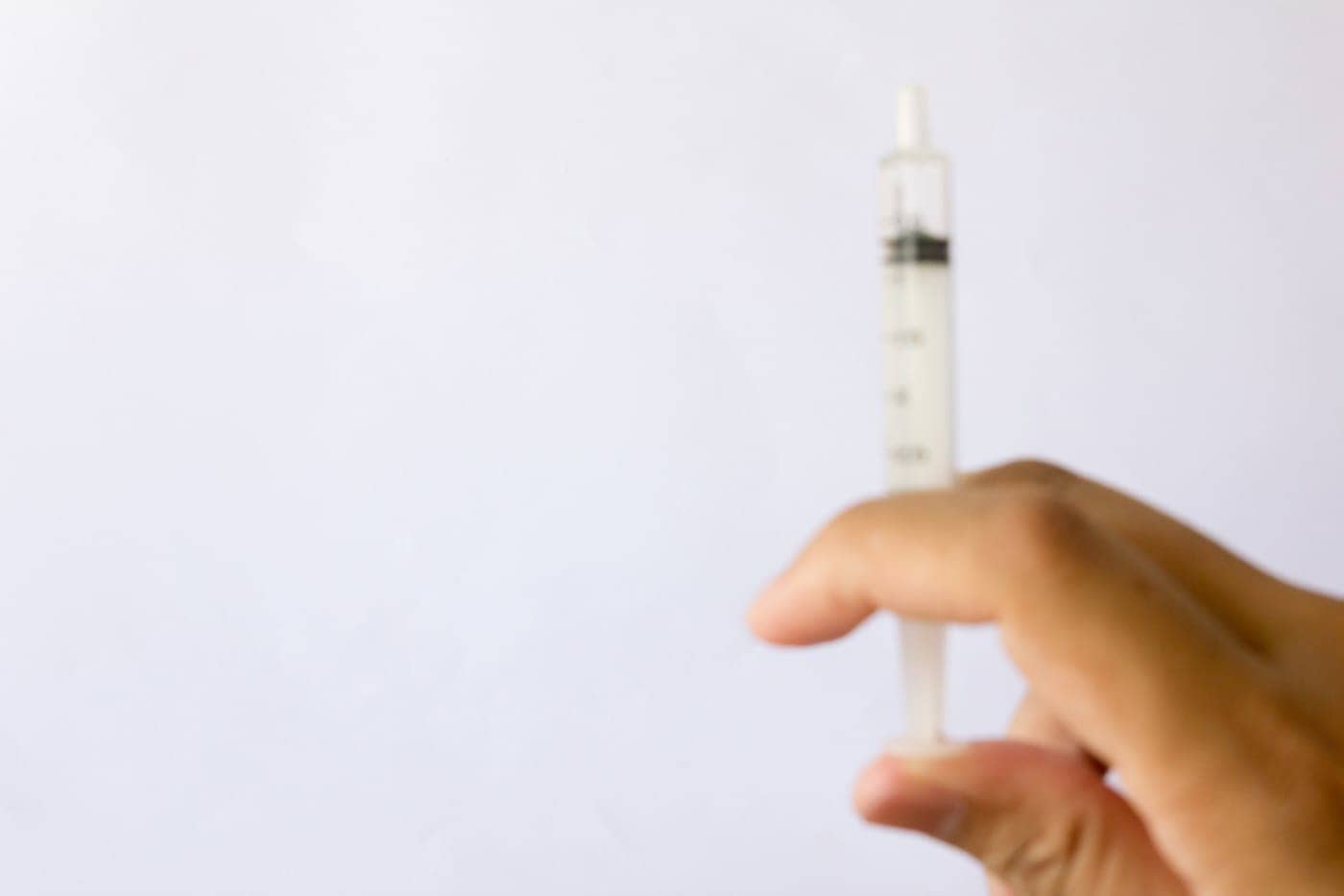 Punción de una jeringa con líquido en fondo blanco, símbolo de salud y medicina.