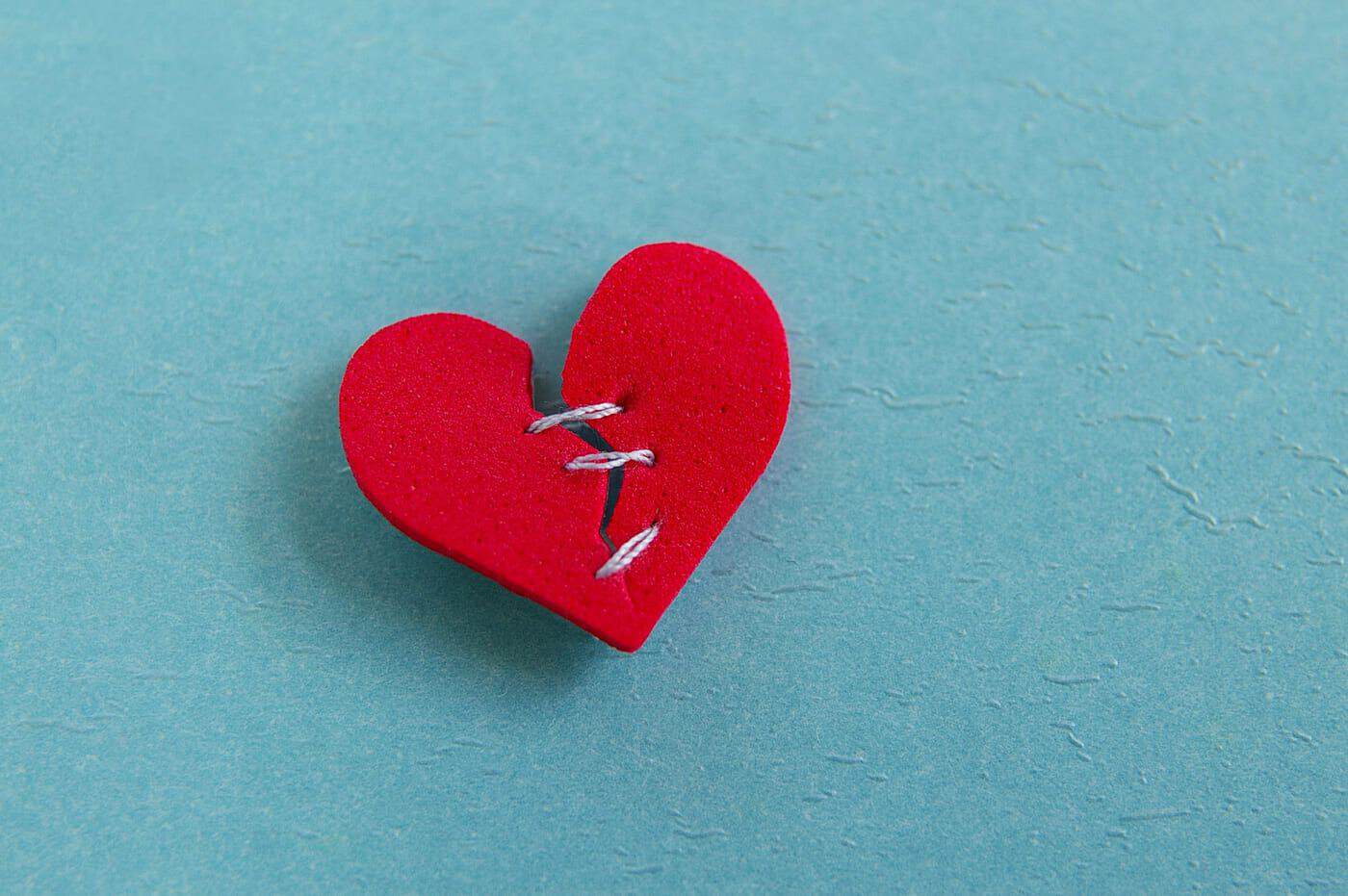 Corazón de felpa roto con costura, simboliza dolor emocional y sanación en filosofía.