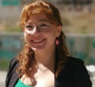 Mujer sonriendo con gafas en un entorno al aire libre.