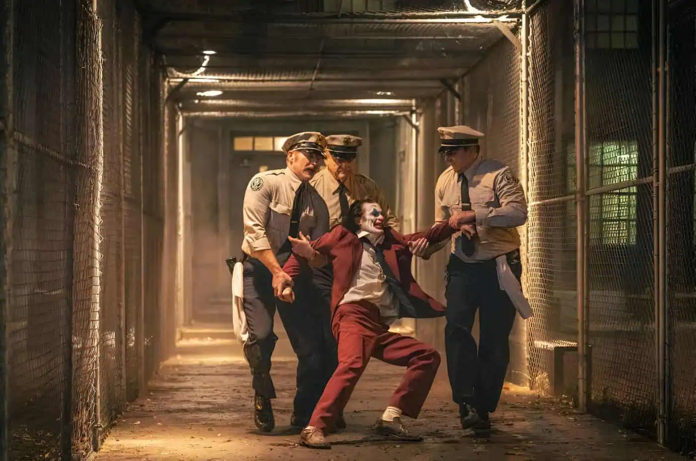 Maestro Joker detenido por policías en un pasillo con rejas, escena de una película de humor.