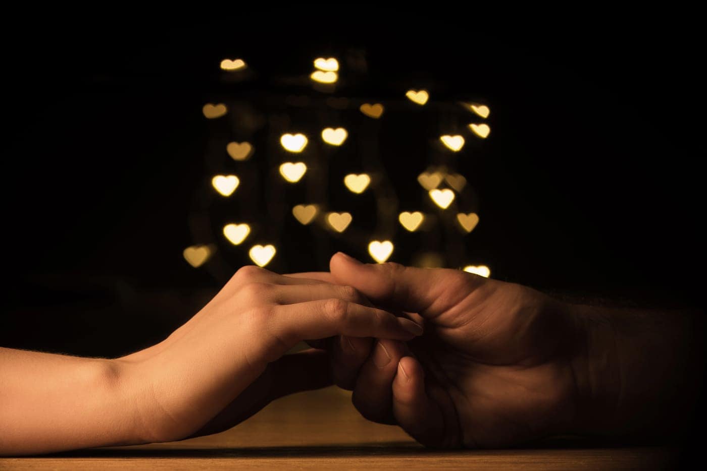 Cuidado y conexión entre manos con luz de corazones en el fondo.