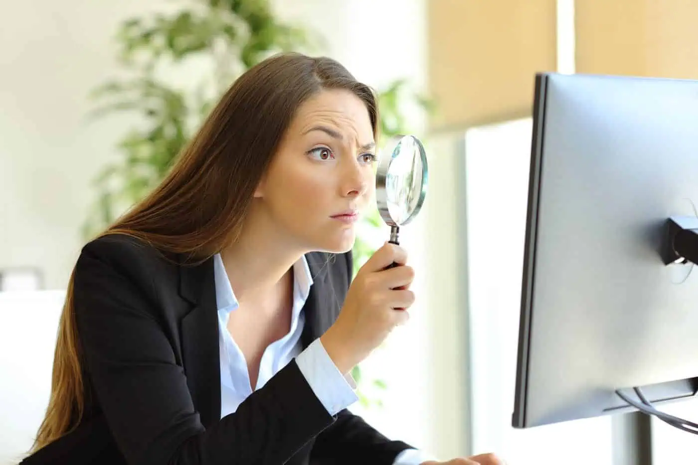 Imagen de una mujer con intriga usando una lupa frente a la computadora, representando la búsqueda de conocimiento filosófico en línea.