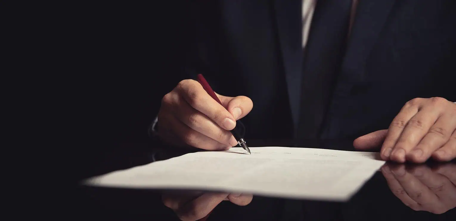 Firma de un documento con una pluma en un entorno oscuro.