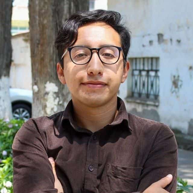 Filósofo joven con gafas frente a pared urbana en exterior.