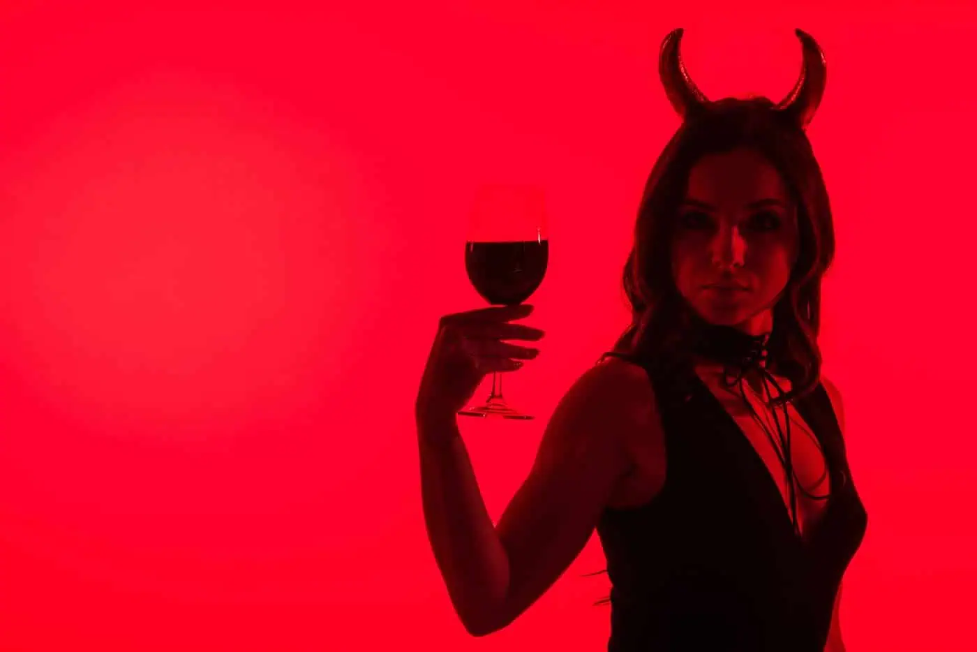 Vampira con cuernos y copa de vino en un fondo rojo oscuro.
