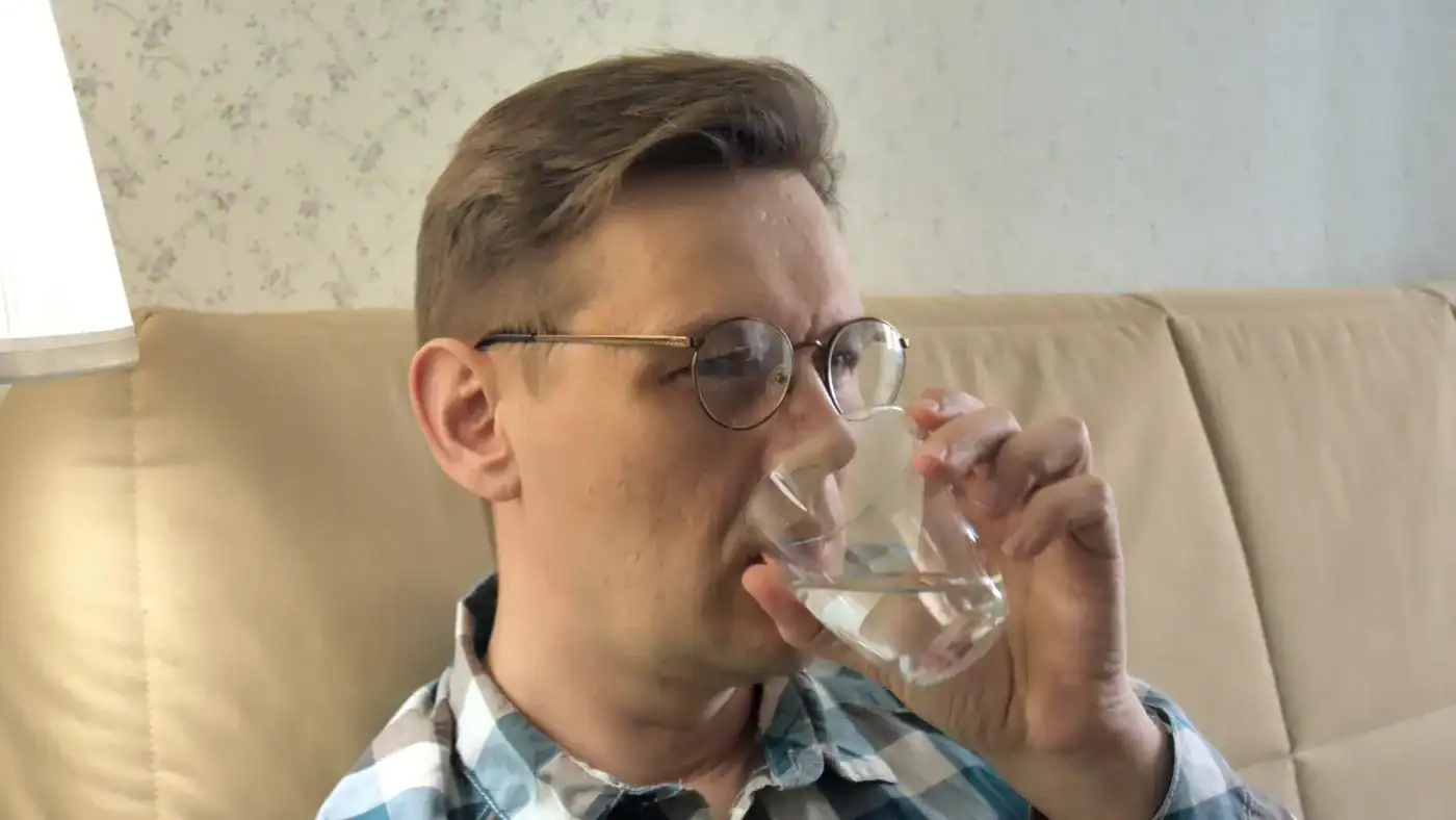 Bebé bebiendo agua, joven con gafas tomando agua, fotografía de un hombre bebiendo agua en un sofá, imagen de un hombre con gafas disfrutando de un momento de hidratación, relevancia.