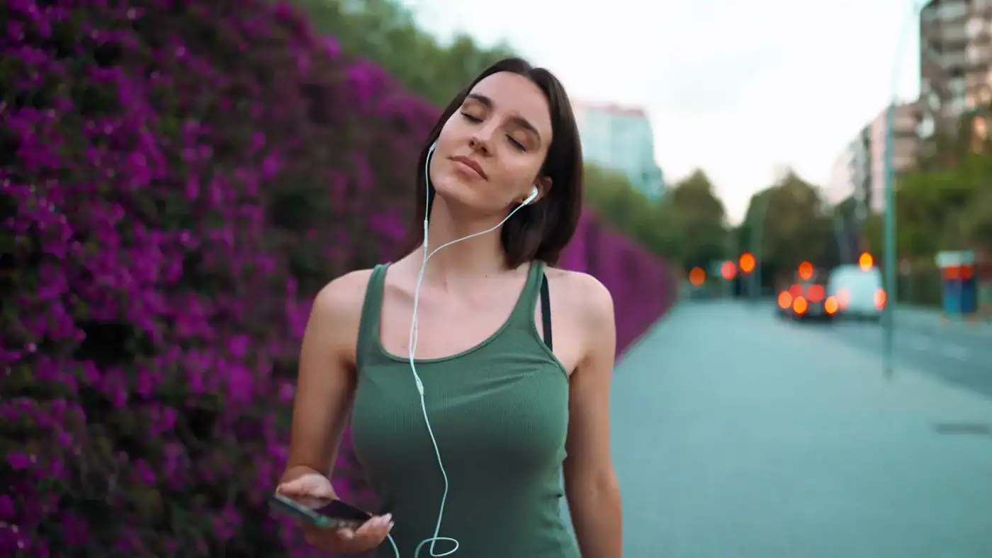 Disfrutando de una caminata al aire libre con música en sus auriculares en un entorno urbano con flores púrpuras.