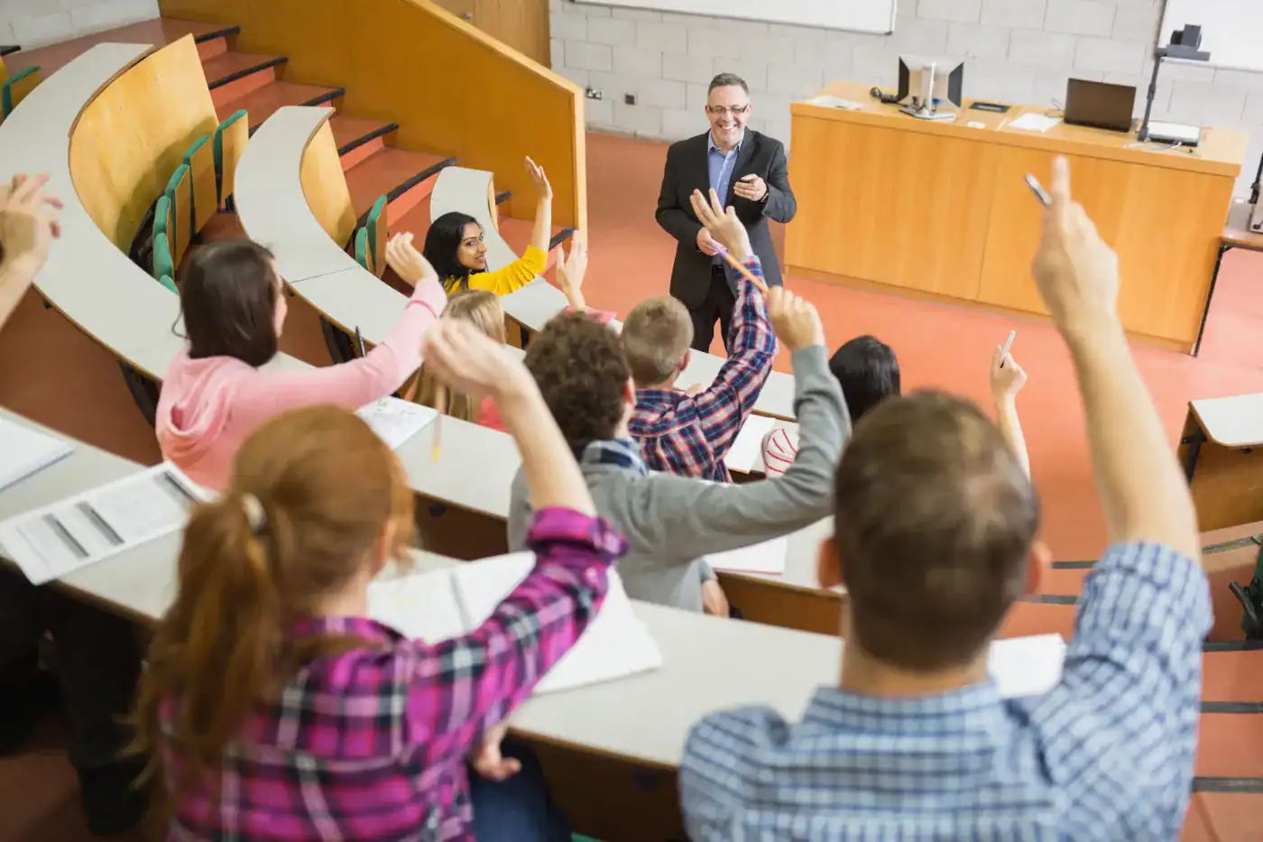 Pregunta a profesor en aula universitaria, estudiantes levantando la mano, enseñanza y participación activa.