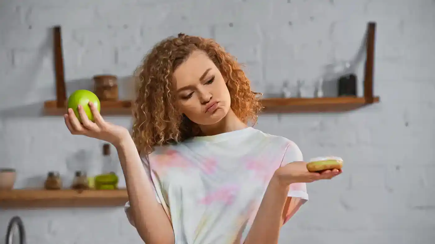Amiga confundiendo una manzana y una dona en la cocina, expresión de confusión.