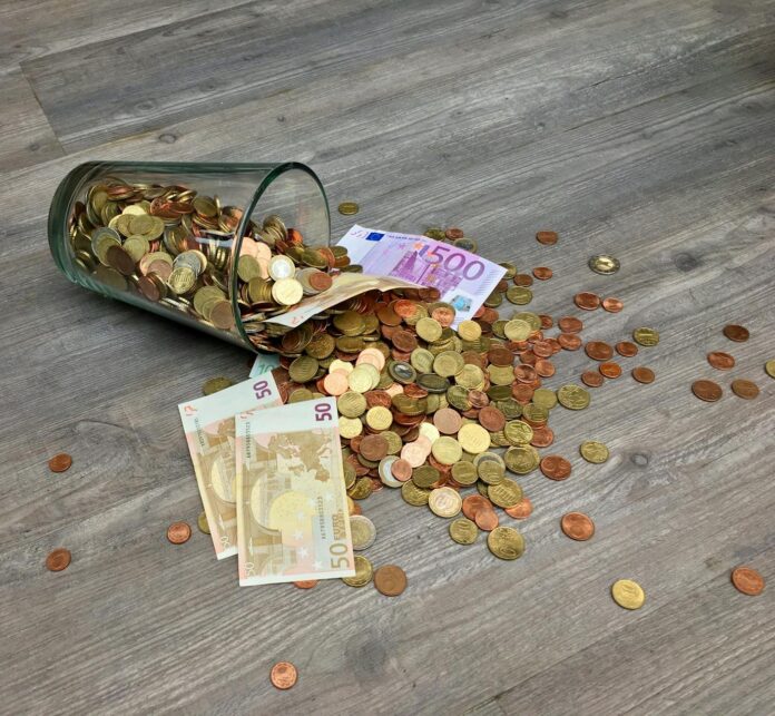 A glass jar with euro coins and banknotes spilled on a wooden surface, representing finance and savi