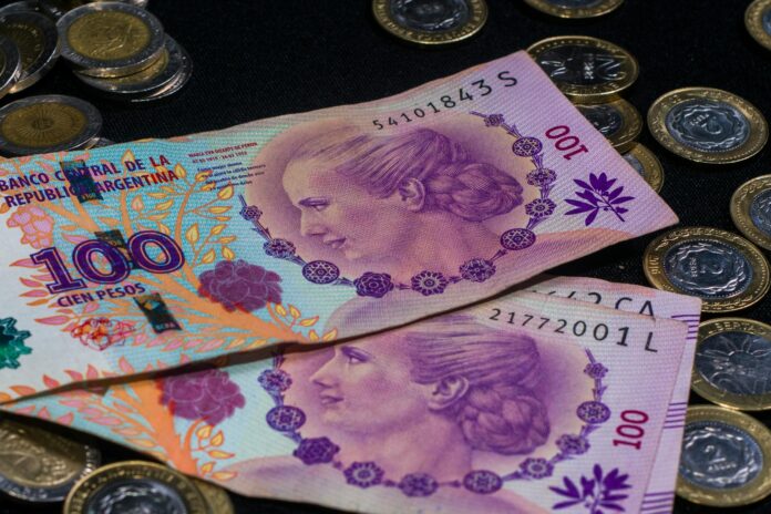 Close-up of colorful Argentine peso banknotes and coins on a dark backdrop.