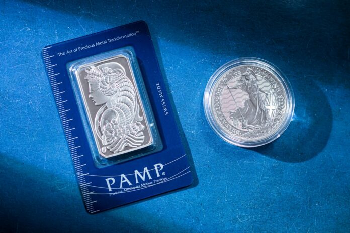 Close-up of a silver coin and a PAMP bar on a blue textured background emphasizing wealth.