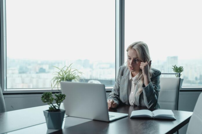 Professional woman engaged in a video meeting at a modern office desk with a laptop.