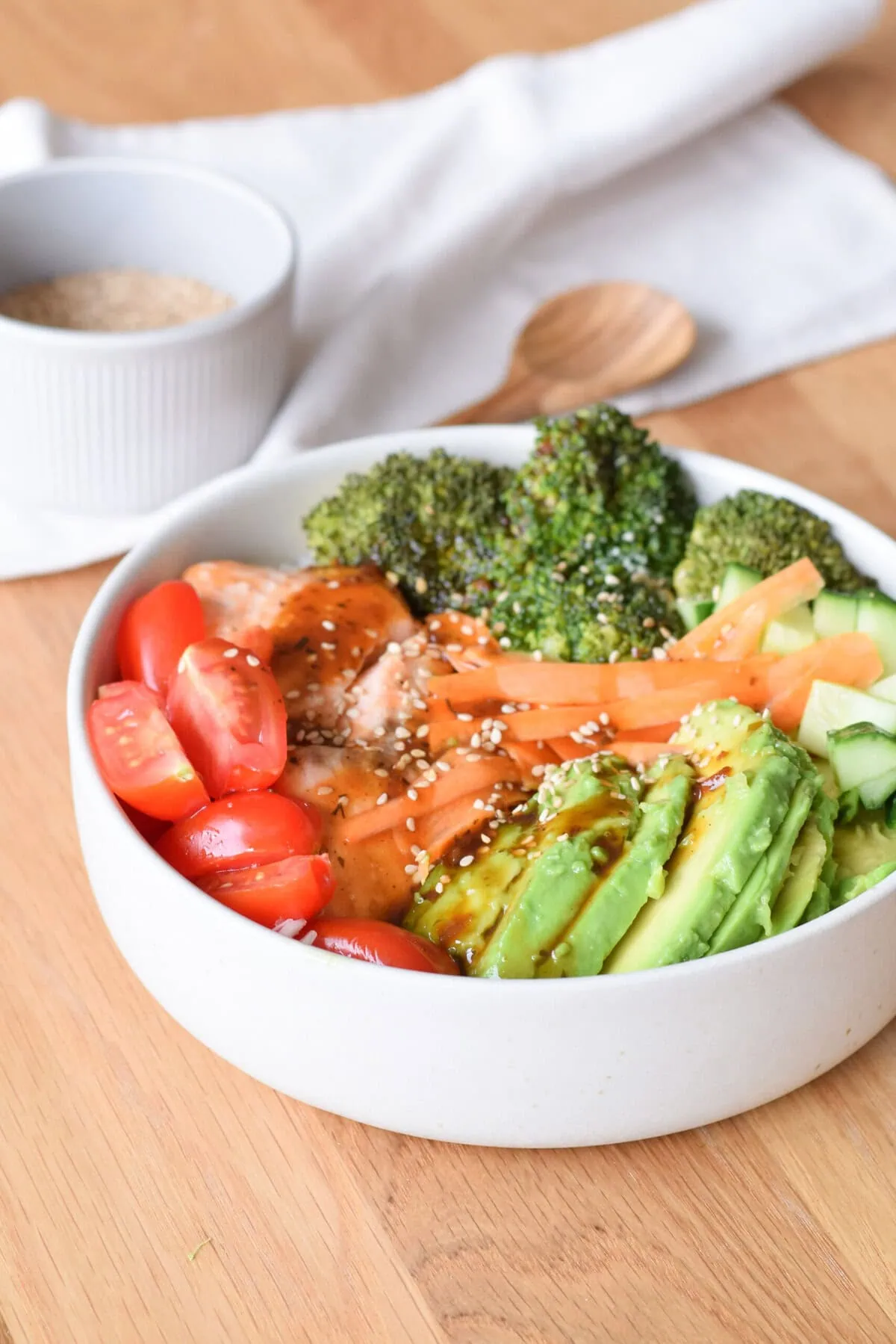 Buddha Bowl mit Tomaten, Brokkoli, Avocado, Karotten und Sesam auf Holz.