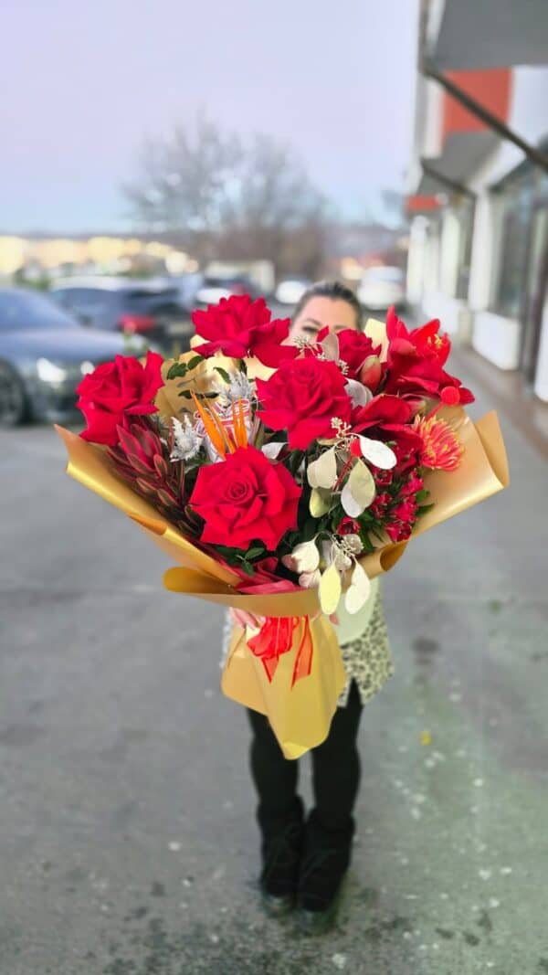 Buchet mixt în nuanțe de roșu și auriu cu trandafiri roșii, amarilis, gerbera, alstroemeria, leucadendron, craspedia, eucalipt auriu și floare decorativă centrală