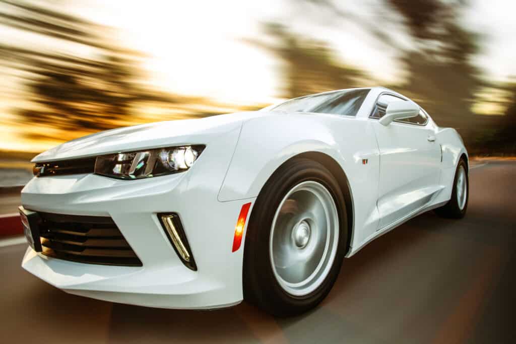 The white chevrolet camaro is driving down the road near John Glenn International Airport.