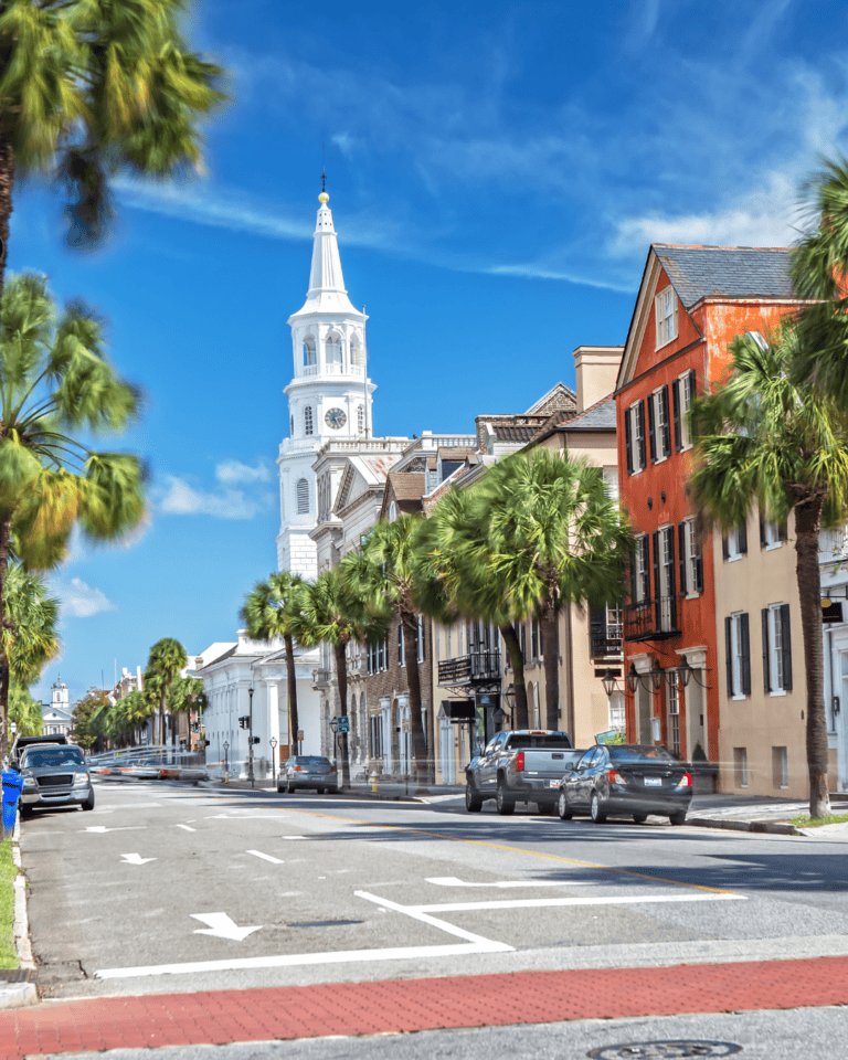 A white historic building stands up above other storefronts on a clear, blue sky day in Charleston, South Carolina.