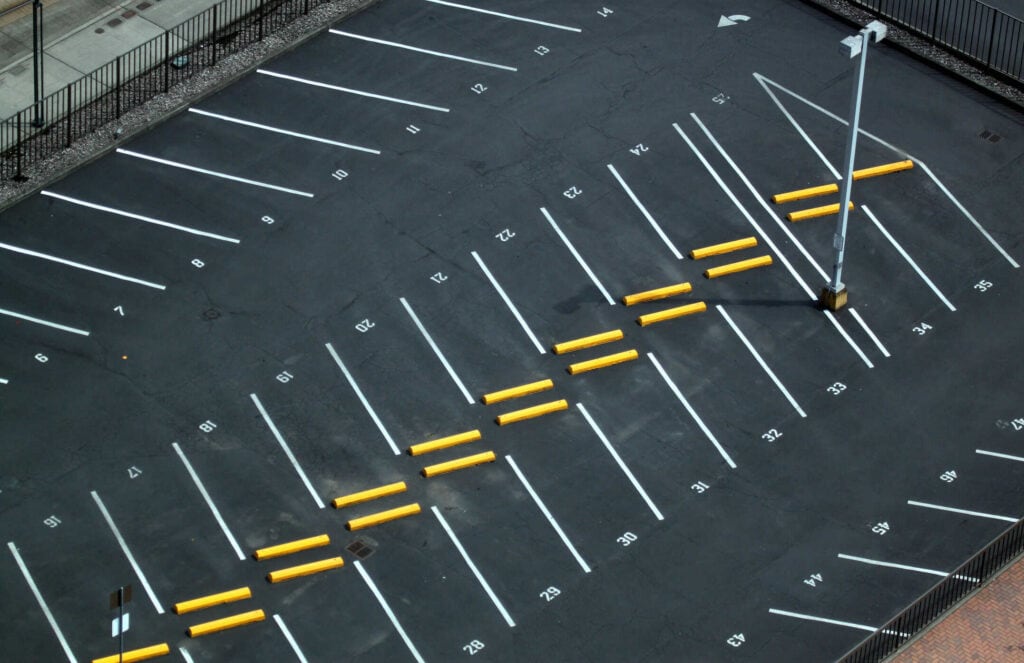 Aerial view of an empty asphalt parking lot with white lines, numbers, and yellow parking blocks.