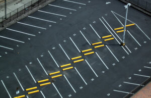 Aerial view of an empty asphalt parking lot with white lines, numbers, and yellow parking blocks.