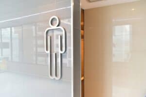 A silver male restroom symbol on a glossy light gray tiled wall.