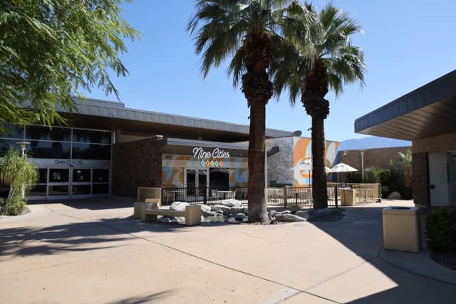 An outdoor plaza with a restaurant named "Nine Cities," palm trees, and a building with "GATES 12 TO 20" signage under a clear blue sky.