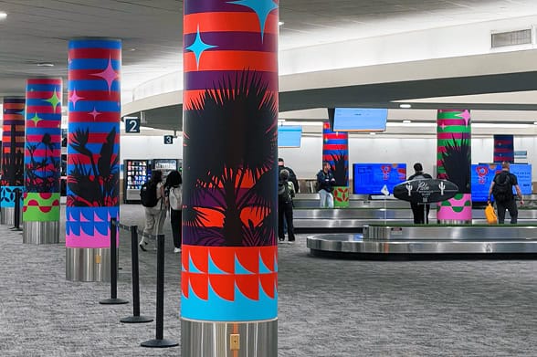 Airport baggage claim area with colorful, tropical-themed pillars, people, and baggage carousels.
