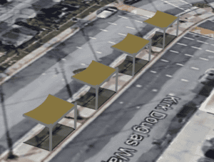 Aerial view of four identical light brown and grey canopy structures lined up along a grey asphalt road with 'Kirk Douglas Way' written on it.