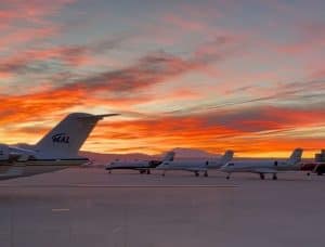 Corporate jets parked at an airport set against an orange sunrise