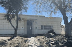 gray, flat roofed building with trees flanking the entrance