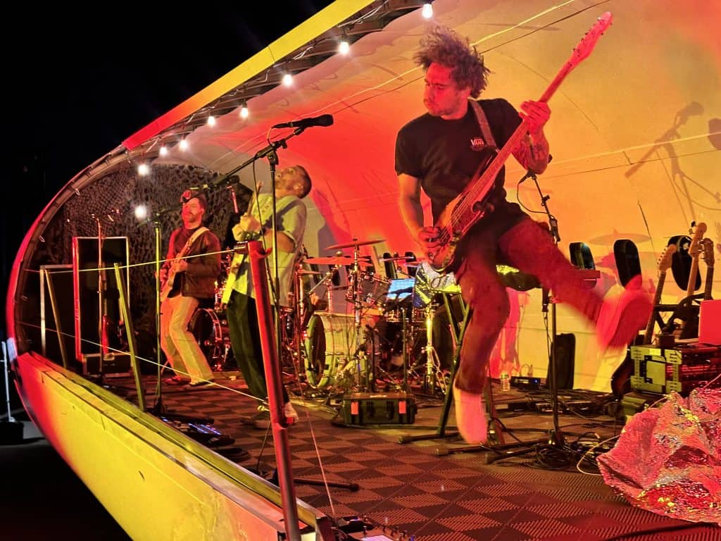 A guitarist leaning back mid-solo on the orange-lit stage inside the open 737 fuselage.