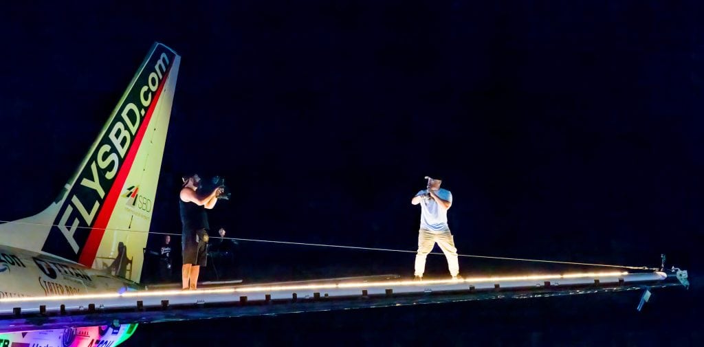 A performer on the floodlit FLYSBD.com wing-level stage at night.