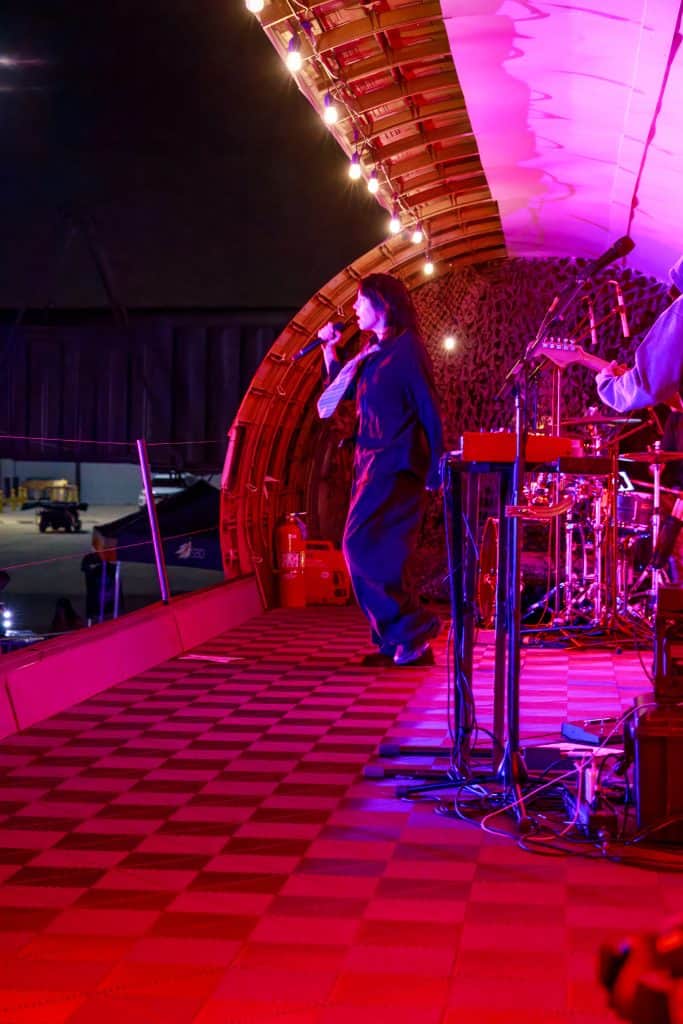 A performer on the magenta-lit Plane Stage at night.