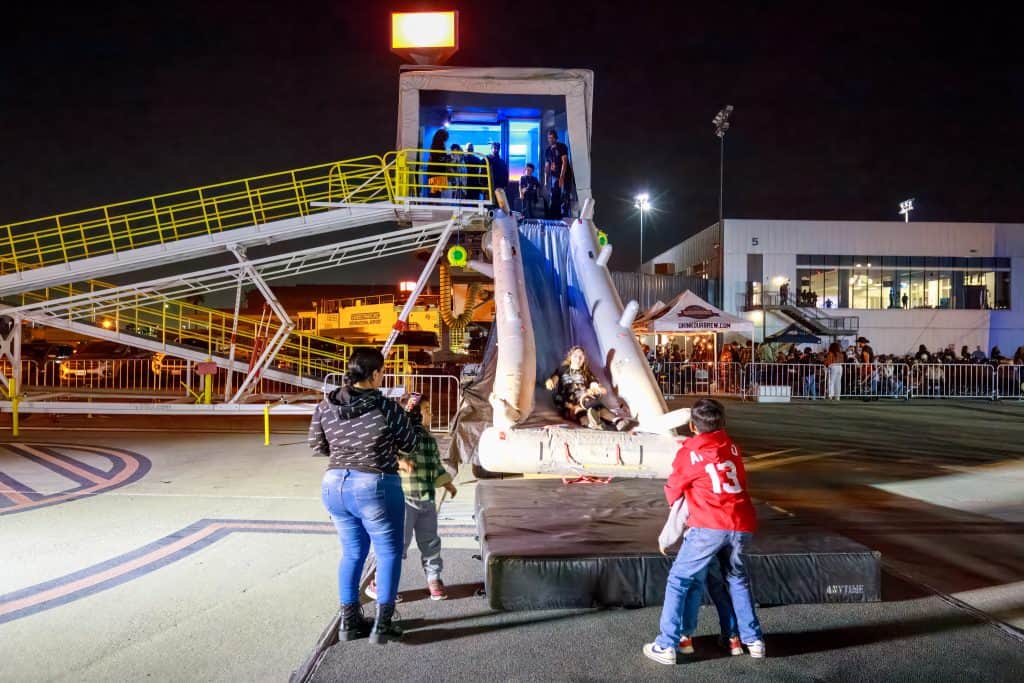 Families queueing for the inflatable slide off the airstair on the tarmac at night.