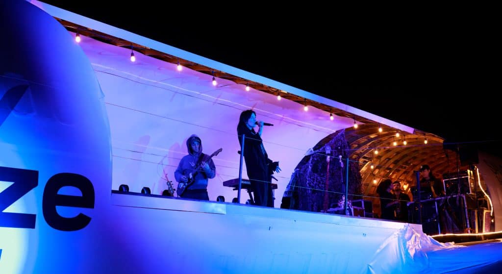 The Breeze-liveried 737 Plane Stage lit in blue at night, with a duo performing on the wing-level stage.