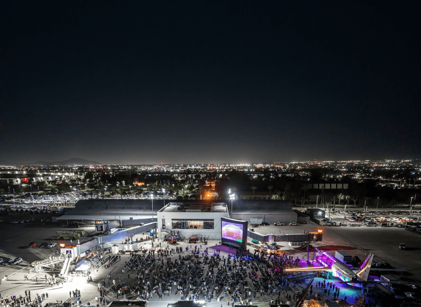 Aerial view of the Cruising at Altitude festival on the SBD tarmac at night, with crowds gathered around the lit Plane Stage.