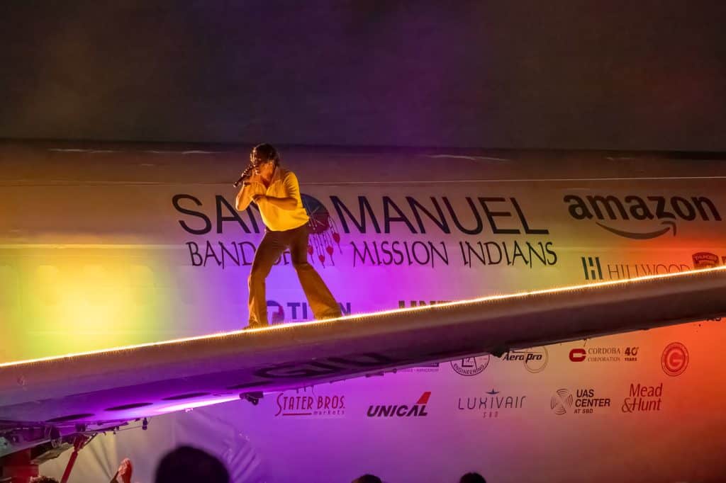 A singer performing on the Plane Stage in front of a San Manuel Band of Mission Indians banner.