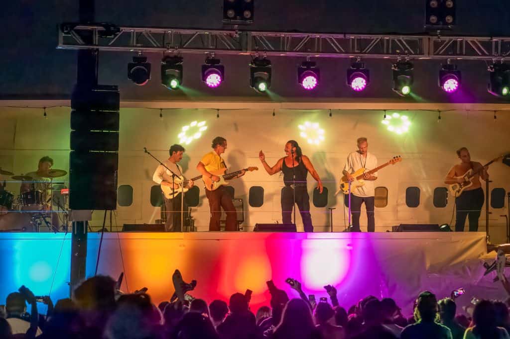 A five-piece band performing on the Plane Stage under coloured lights.