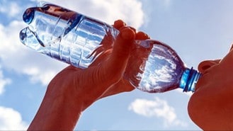 Clean water being poured from a plastic bottle in a clear sky.