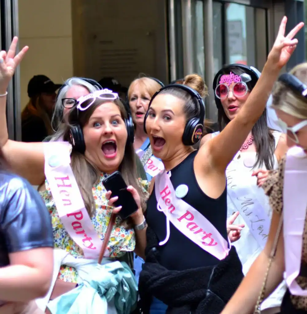 Group of women enjoying a silent disco with headphones and sashes at a party.